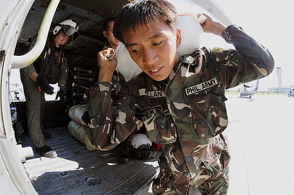 A soldier from the Armed Forces of the Philippines carries a 100-pound bag of rice to a helicopter assigned to the 