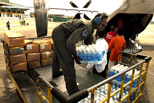 Aviation Structural Mechanic 2nd Class Myron Robertson, of Carson, Calif., stacks supplies onto a cart at Kalibo Airport while a C-2A Greyhound is unloaded. The supplies, delivered by the 