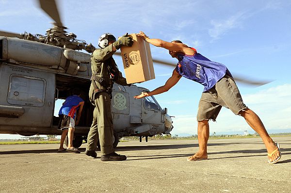 Aviation Warfare Systems Operator 2nd Class Slavek Glownia and a villager from Kalibo move a box of humanitarian supplies from an SH-60F Seahawk flown by members of Helicopter Anti-Submarine Squadron (HS) 4.