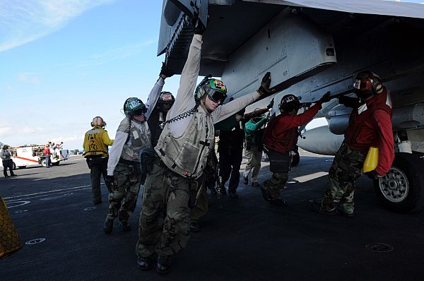 Flight deck personnel push back an F/A-18C Hornet assigned to the 