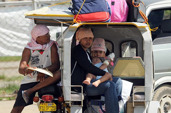 People sit outside the gates of the airport in Kalibo as supplies from the Nimitz-class aircraft carrier USS Ronald Reagan (CVN 76) arrive via helicopter to the devastated region after Typhoon Fengshen.